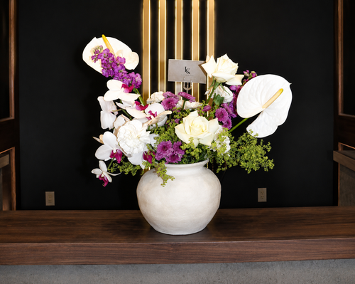 Moonlit Garden arrangement by Lenorah & Co. — ivory garden roses, white anthurium and cascading phalaenopsis orchids with violet stock in a hand-textured plaster vessel.
